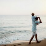 Father with a toddler boy walking on beach on summer holiday, having fun.